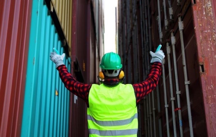 person in ppe with arms raised at cargo containers